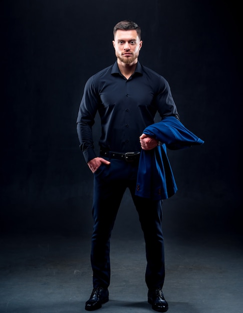 Portrait of handsome young successful man wearing dark shirt. Man holding dark blue jacket. Black background. business concept.