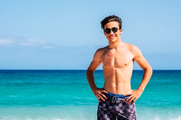 Portrait of handsome young teenager caucasian man smile and enjoy the summer holiday vacation at the beach with blue water and sky in scene