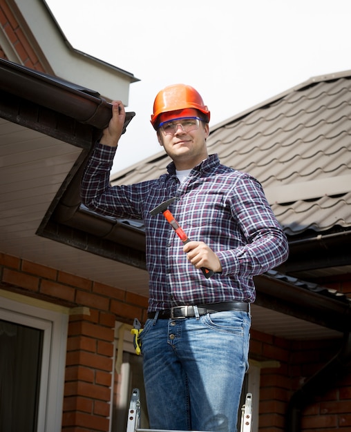 Portrait of handyman standing on high ladder and inspecting house roof