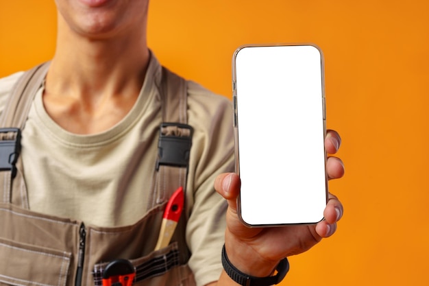 Portrait of handyman in uniform showing blank mobile phone on yellow background