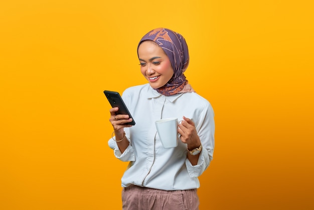 Portrait of happiness Asian woman relaxing holding mug and using mobile phone over yellow background