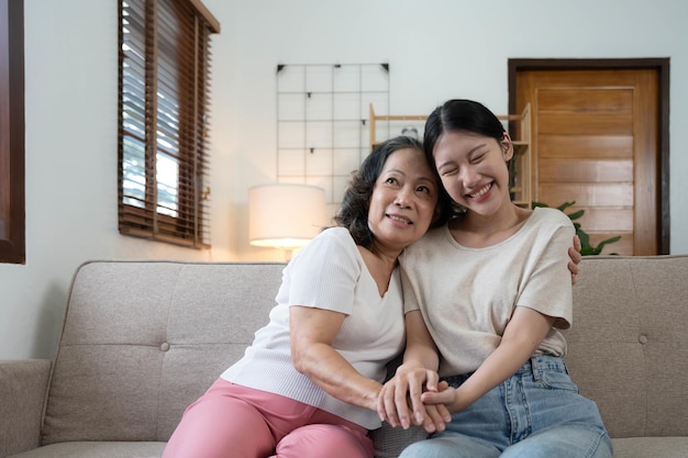 写真 portrait happy adult daughter and older mother hugging and holding hands sitting on couch at home young woman and mature mum or grandmother looking at camera two generations family photo