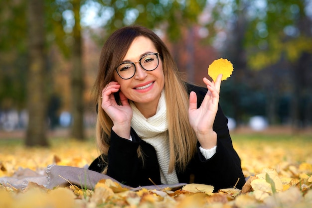 幸せな大人の中年熟女の肖像画、眼鏡をかけた美しい女性が公園で横たわっている