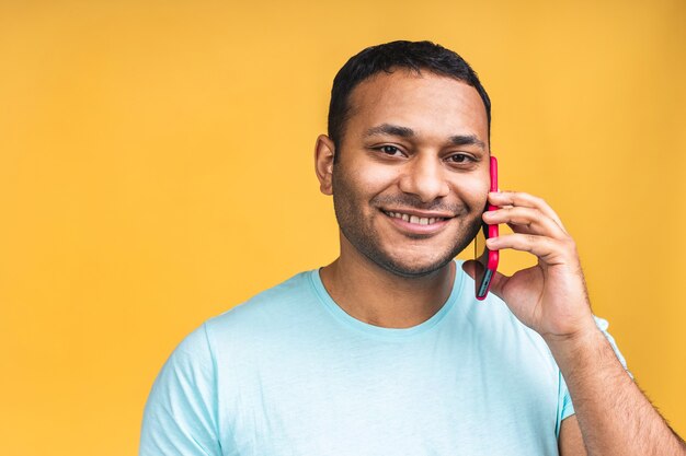 Ritratto di un uomo indiano nero afroamericano felice che parla sul telefono cellulare isolato sopra fondo giallo.