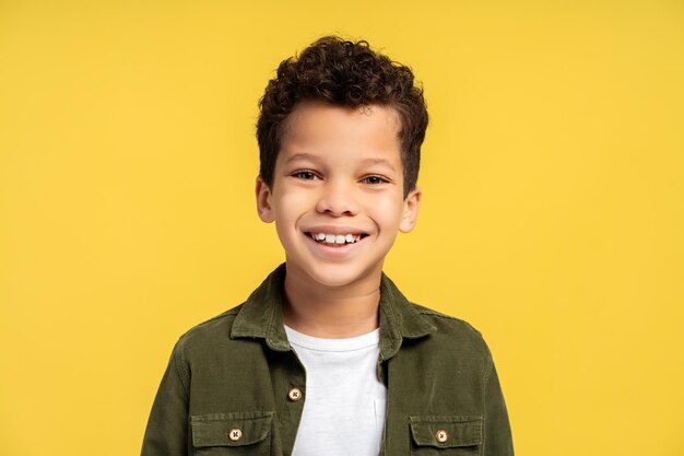 Portrait happy African American boy looking at camera while posing isolated on yellow background