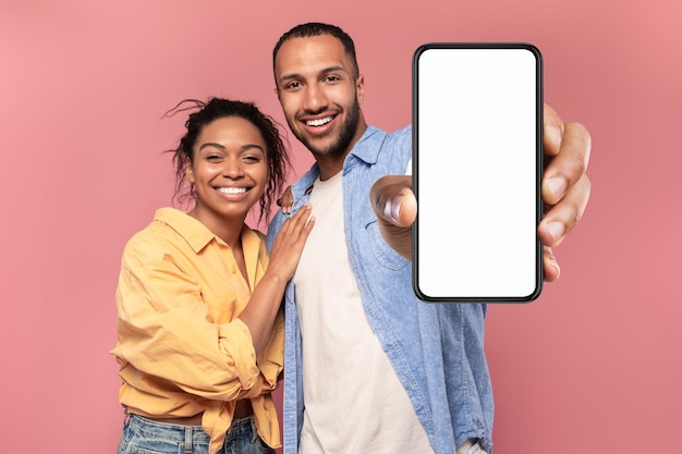 Portrait of happy african american couple presenting cellphone with mockup promoting app or website