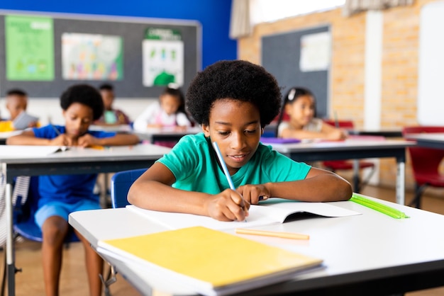 幸せなアフリカ系アメリカ人の小学生が授業の机でノートブックで書いている肖像画