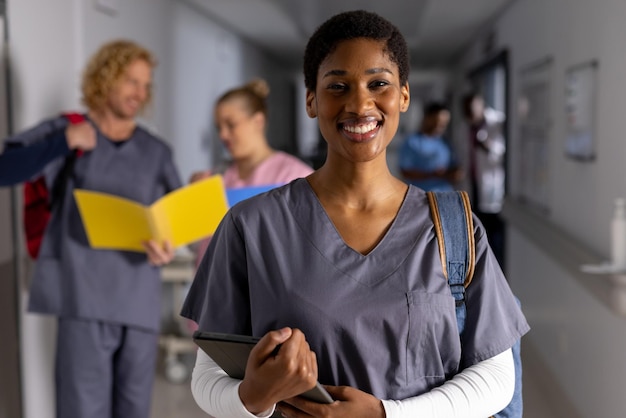 행복 한 아프리카계 미국인 여성 의사 의 초상화 는 병원 의 복도 에서 태블릿 을 들고 스크럽 을 입고 있다