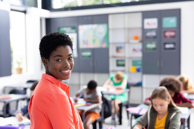 Photo portrait of happy african american female teacher in classroom with diverse pupils copy space