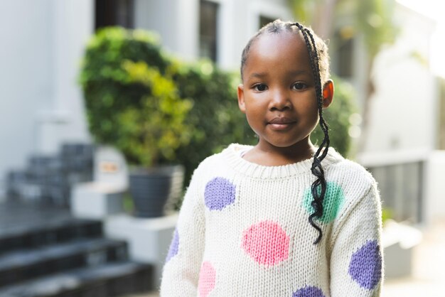 Portrait of happy african american girl with braids standing outside house copy space