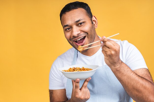 パスタを調理する幸せなアフリカ系アメリカ人のインドの黒人シェフの肖像画。料理、職業、高級料理、食べ物、人々の概念は黄色の背景の上に分離されました。