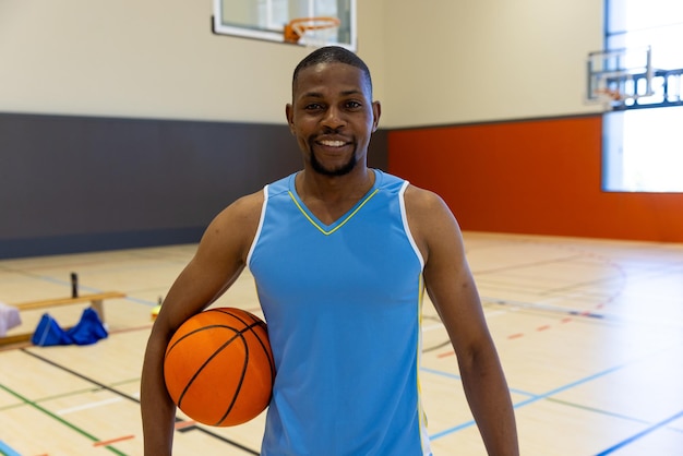 Портрет счастливого афроамериканского баскетболиста в синей спортивной одежде в спортзале. Спорт, активность и образ жизни, неизменны.