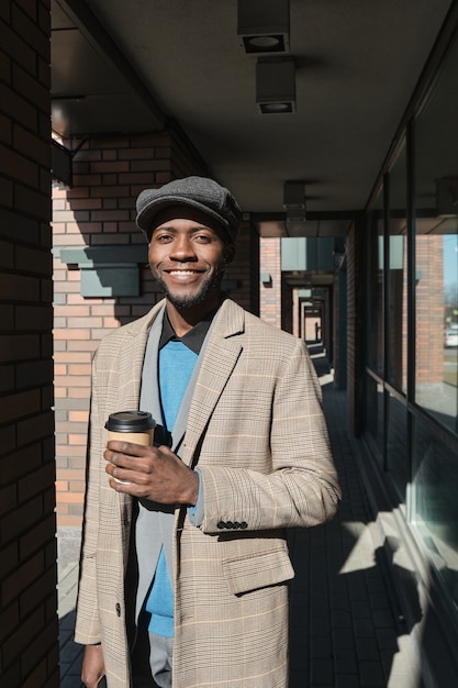 카메라를 보고 웃고 야외에서 커피를 마시는 행복한 아프리카 남자의 초상화