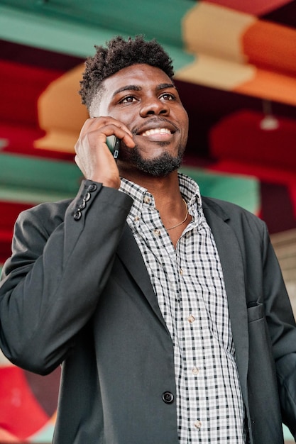 Portrait of a happy AfricanAmerican man talking on a smartphone with a colourful city background