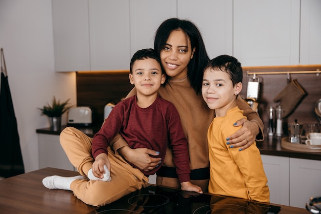 キッチンで幸せなアフリカ系アメリカ人の家族、お母さんとカメラを見ている2人の息子の肖像画。高品質の写真