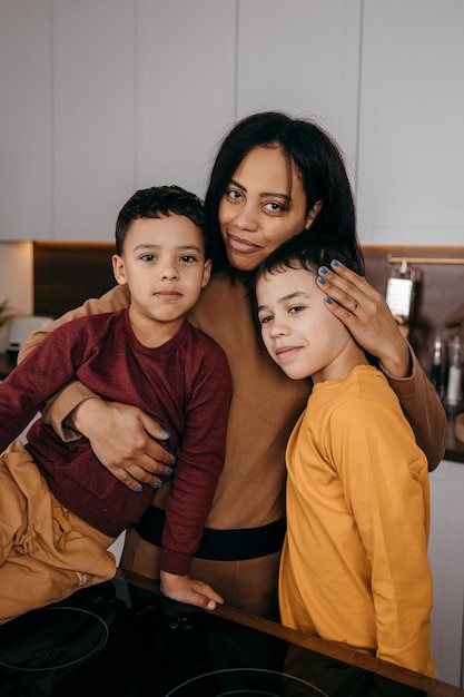 キッチンのお母さんとカメラを見ている2人の息子の幸せなアフリカ系アメリカ人の家族の肖像画
