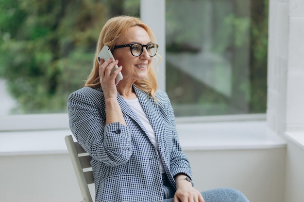 Portrait of happy aged businesswoman in glasses talk on smartphone consulting client online smiling senior woman speak on cellphone use wireless connection Technology concept