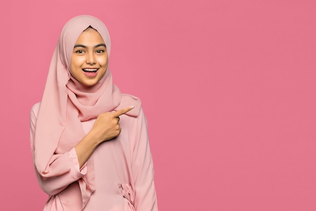 Portrait of happy amazed young Asian woman pointing with finger to copy space