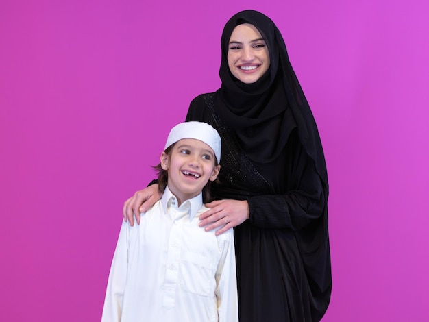 portrait of happy arabian family muslim mother and son wearing traditional clothes isolated over pink background