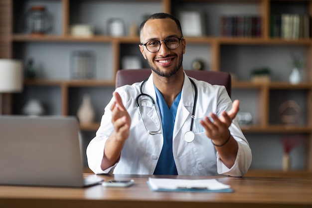 Portrait of happy arabic doctor sitting at workdesk at clinic