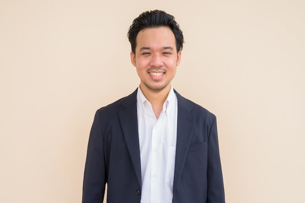 Portrait of happy Asian businessman wearing suit against plain background