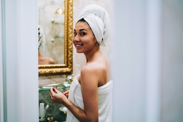 Portrait of happy asian female model in white towel smiling at camera during morning time for refreshing and showering in bathroom carefree young woman posing while relaxing in home interior