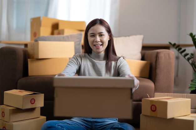 Portrait happy asian female online store small business owner\
entrepreneur packing package post shipping box preparing delivery\
parcel on table ecommerce dropshipping shipment service\
concept