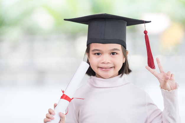 Portrait happy Asian female school kid graduate in a graduation cap holds a rolled certificate. Graduation Celebration Concept Stock Photo