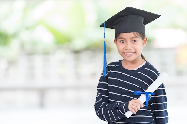 Portrait happy asian female school kid graduate in a graduation\
cap holds a rolled certificate. graduation celebration concept\
stock photo