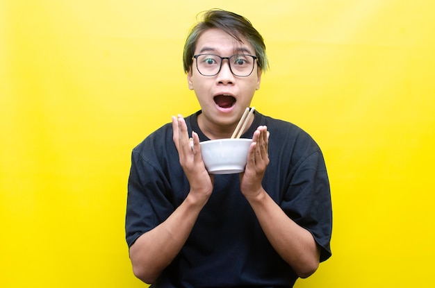 Portrait of Happy Asian man in black tshirt eats instant noodles using chopsticks and bowl isolated