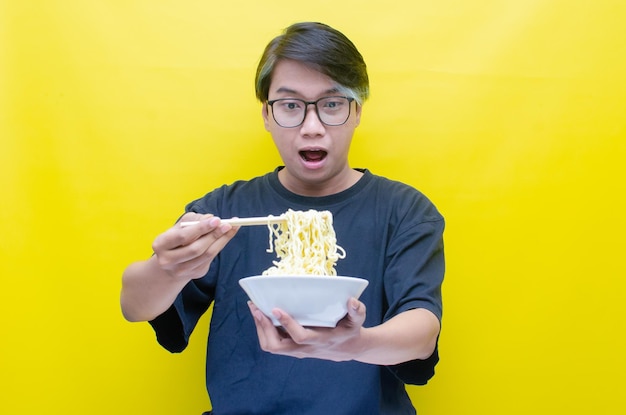 Portrait of Happy Asian man in black tshirt eats instant noodles using chopsticks and bowl isolated