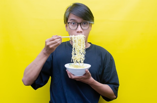 Portrait of Happy Asian man in black tshirt eats instant noodles using chopsticks and bowl isolated