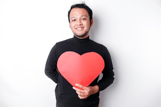 A portrait of a happy Asian man wearing a black shirt holding a red heartshaped paper isolated by white background