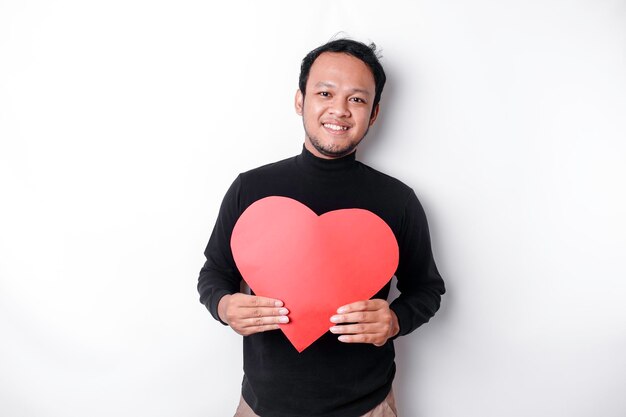 A portrait of a happy Asian man wearing a black shirt holding a red heartshaped paper isolated by white background