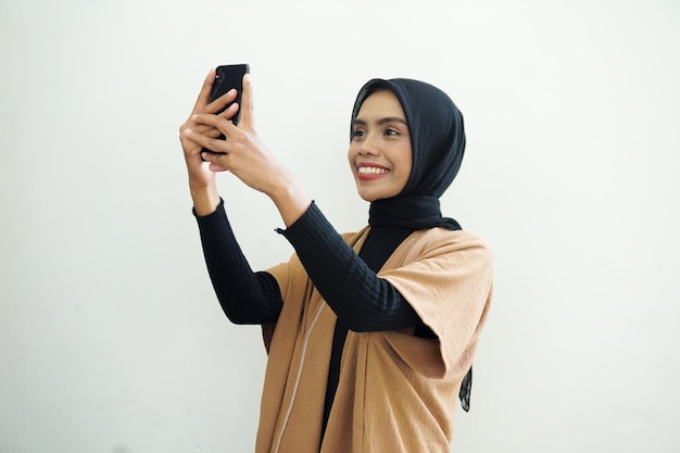 Портрет счастливой азиатской мусульманки в хиджабе, делающей селфи с телефоном