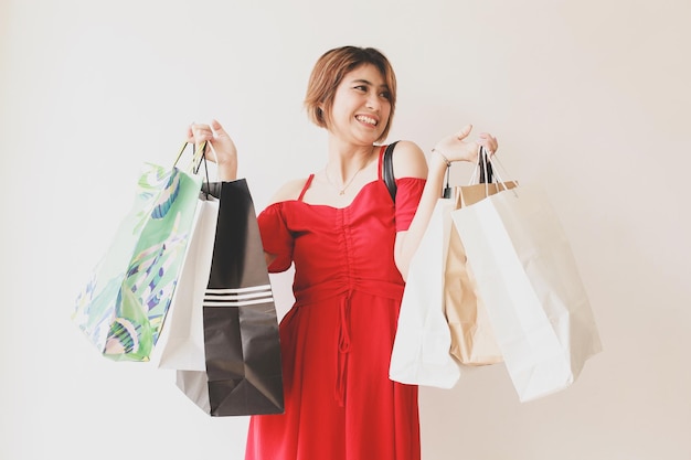 Портрет счастливой азиатской красивой женщины в платье, держащей сумки с покупками с улыбающимся выражением лица и
