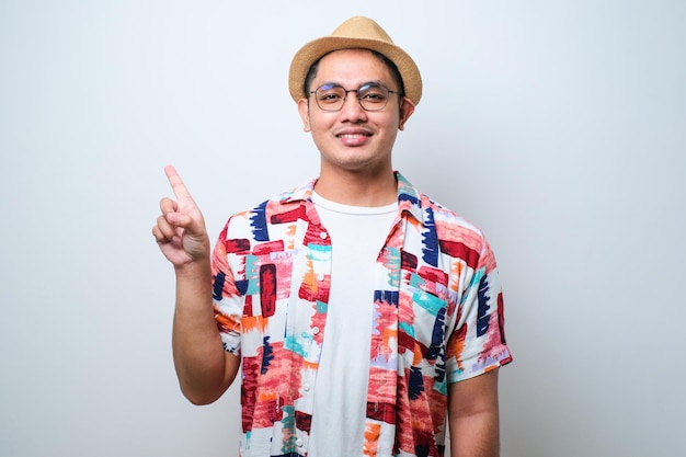 Portrait of happy Asian tourist in casual shirt bucket hat and trendy sunglasses standing and pointing something with finger Traveling holiday trip summer vacation concept