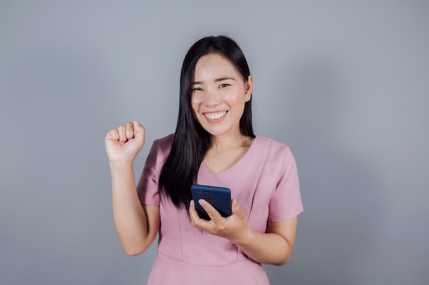 Портрет счастливой азиатки с мобильным телефоном или смартфоном на сером фоне