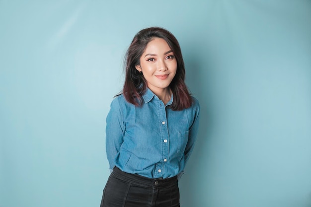 A portrait of a happy Asian woman is smiling and wearing a blue shirt isolated by a blue background