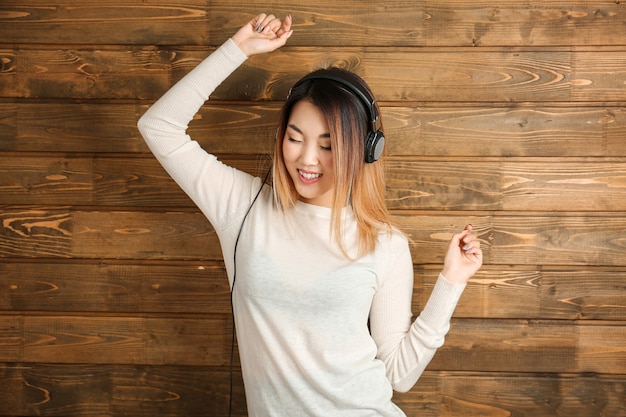 Portrait of happy Asian woman listening to music against wooden