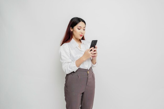 A portrait of a happy Asian woman wearing a white shirt and holding her phone isolated by white background