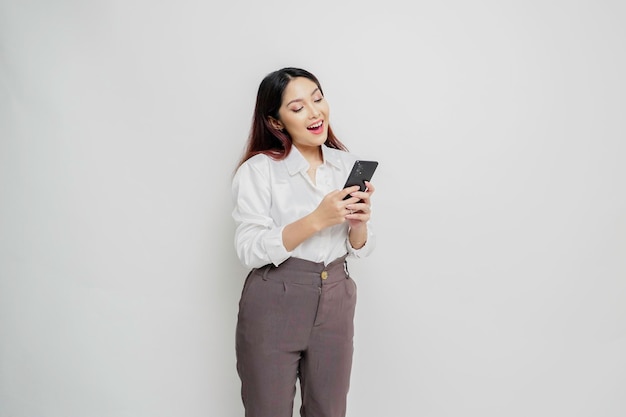 A portrait of a happy Asian woman wearing a white shirt and holding her phone isolated by white background