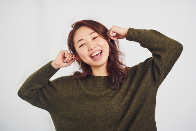 Портрет счастливой азиатской молодой девушки, которая стоит в помещении в студии на белом фоне.