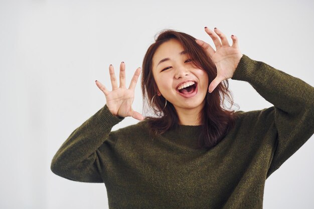 Ritratto di felice ragazza asiatica che sta al chiuso in studio su sfondo bianco.