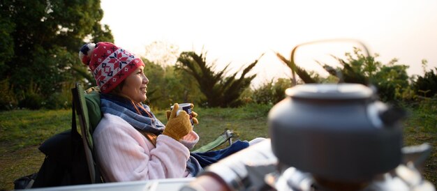 Photo portrait of happy asian young woman in winter costume sitting and drinking hot tea on the mountain