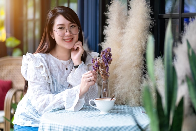 幸せな魅力的なアジアの人々の肖像紫の花の匂いがするかわいい女性コーヒーカップとラベンダーの花束は、背景のようにコーヒーショップでリラックスしたように感じました