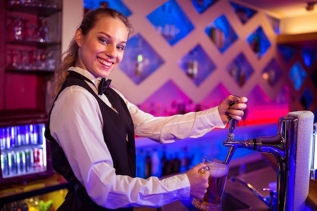 Portrait of happy barmaid pouring beer in glass