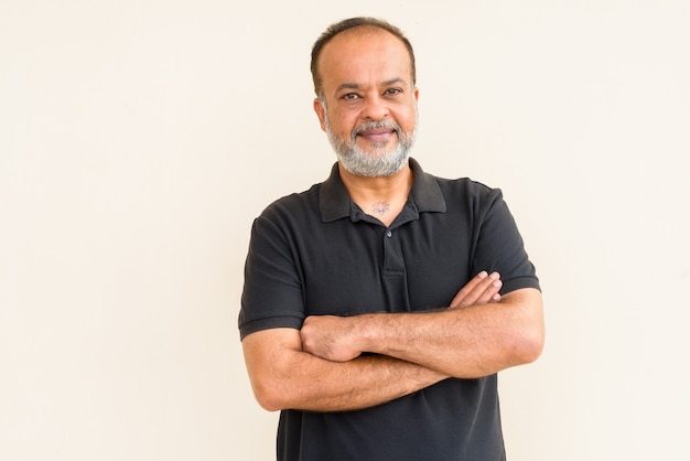 Portrait of happy bearded Indian man smiling against plain wall