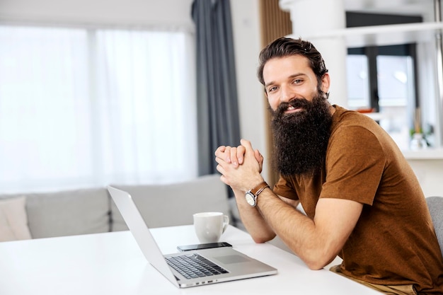 Portrait of a happy bearded man sitting at his cozy home with his laptop