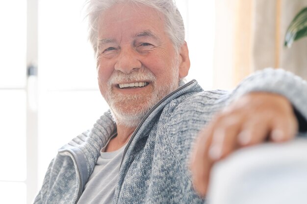 カメラの笑顔を見て自宅のソファでリラックスした幸せなひげを生やした年配の男性の肖像画引退を楽しんでいる年配の魅力的な男性のヘッドショット